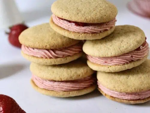 stacked strawberry sandwich cookies next to strawberries.